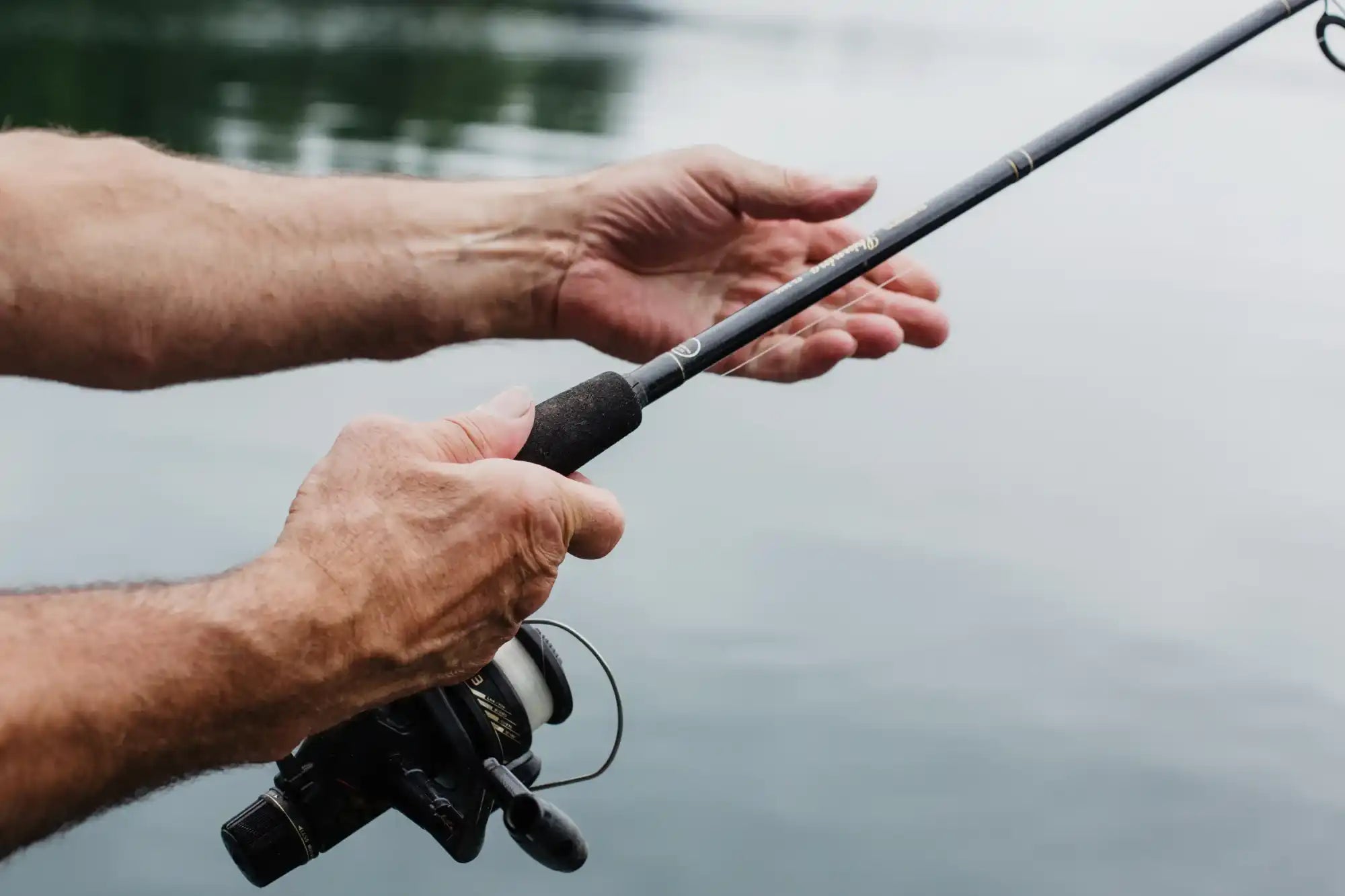 Hands holding a fishing rod with a reel.